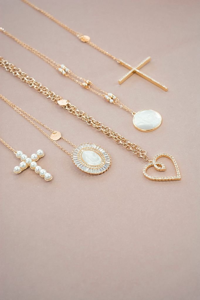 A collection of elegant gold necklaces and pendants artfully arranged on a soft pink background.